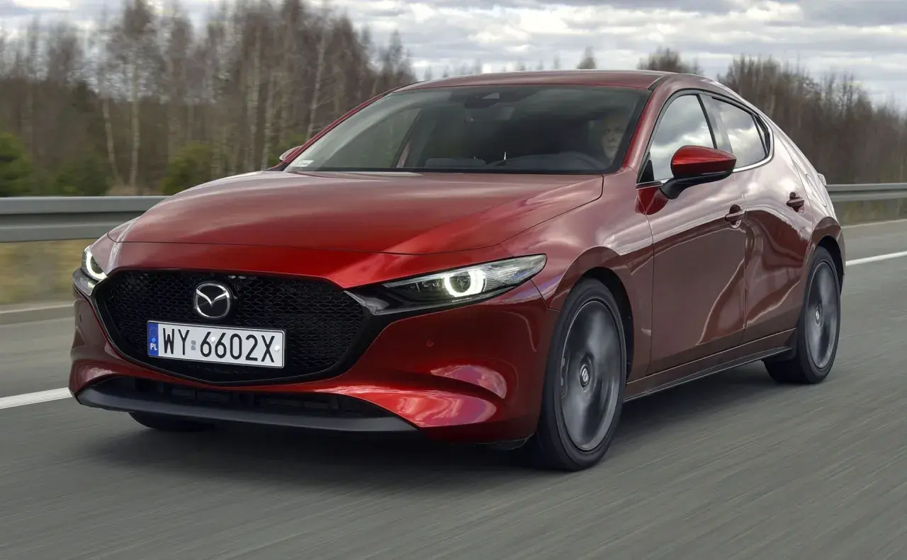 Czerwona Mazda 3 2.0 150KM w ruchu. Kierowca za kierownicą, dynamiczna jazda po drodze.