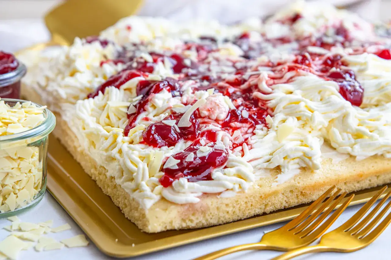 Ein köstlicher Spaghetti-Kuchen vom Blech, verziert mit Sahne, Kirschen und weißen Schokostreuseln.