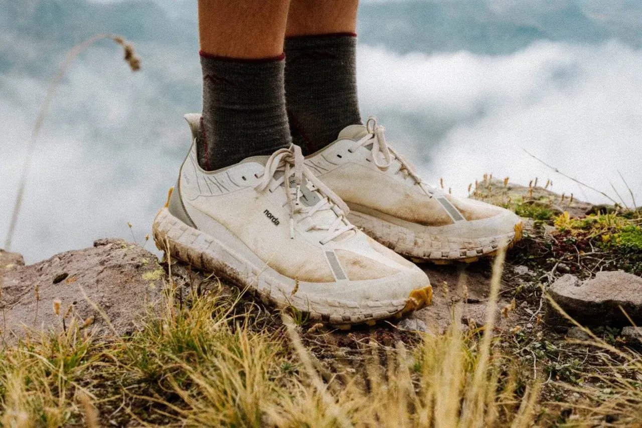 A pair of well-worn, white norda 001a trail running shoes stand on a rocky, grassy peak, ready for adventure.