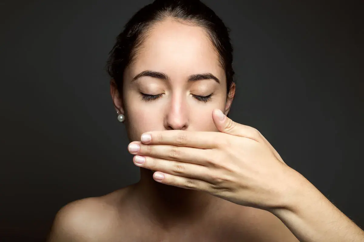 Donna con mano sulla bocca, occhi chiusi, come se avesse scoperto che il filo interdentale puzza.