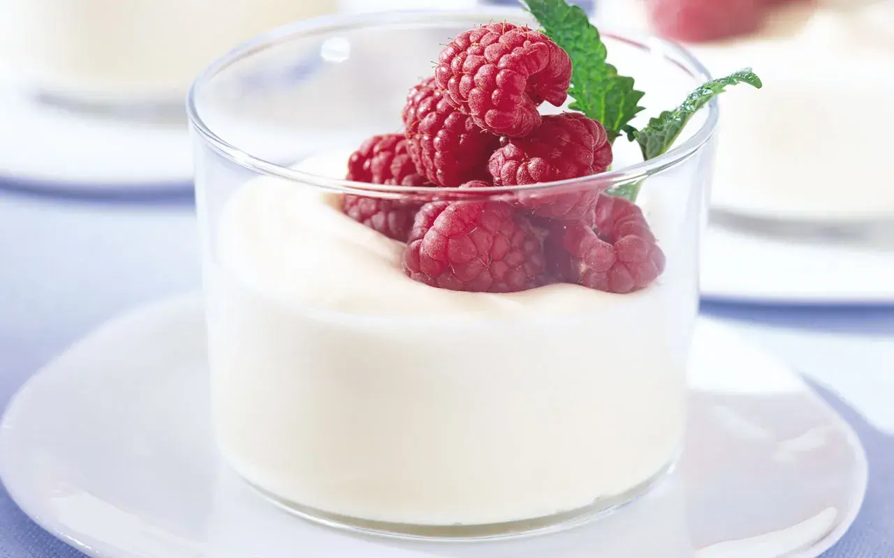 En len vit chokladmousse toppas med färska hallon och en myntakvist i ett glas.