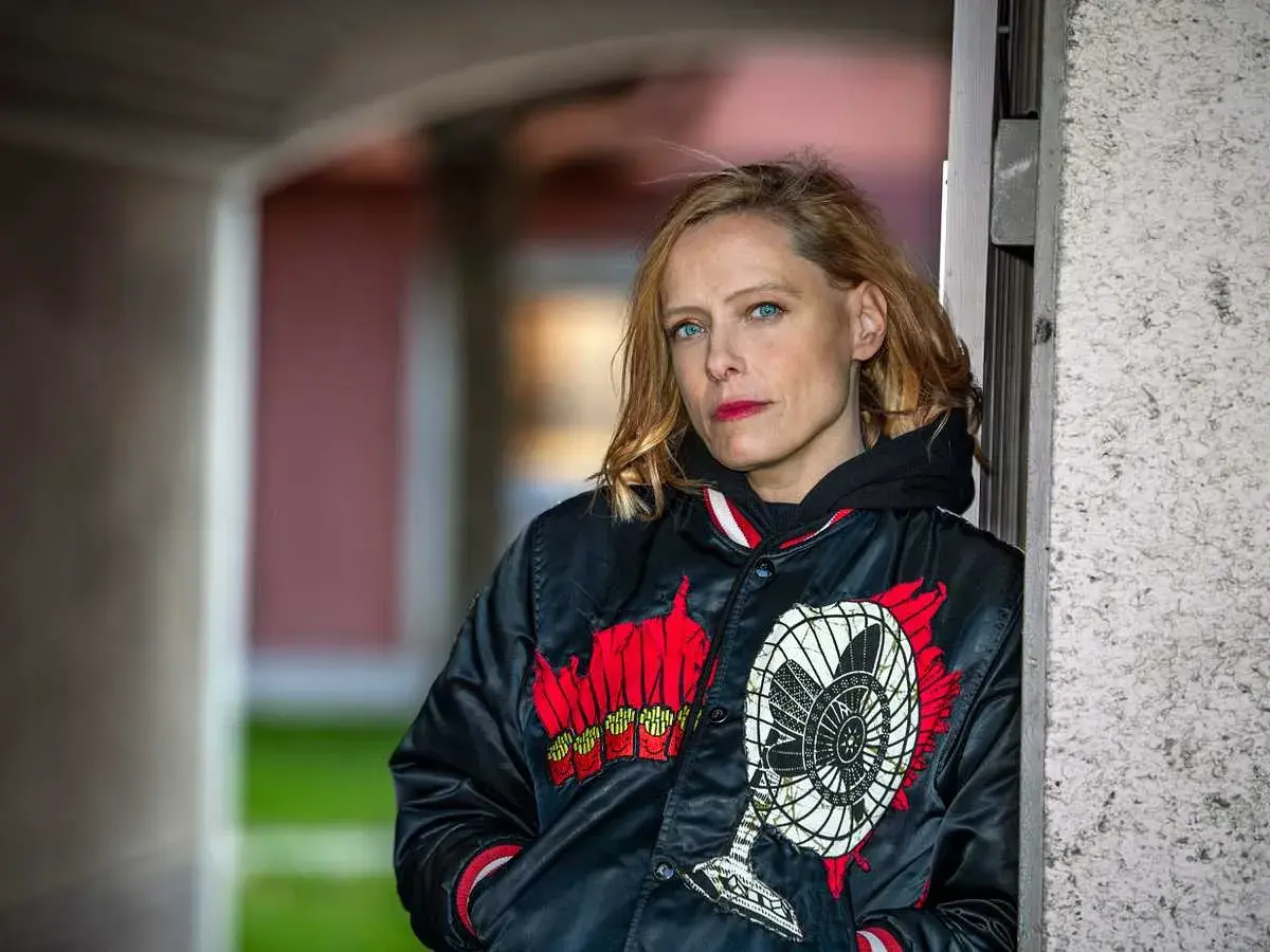 Wanda Bendjelloul, med blå ögon och rött läppstift, bär en svart jacka med en fläkt-design.