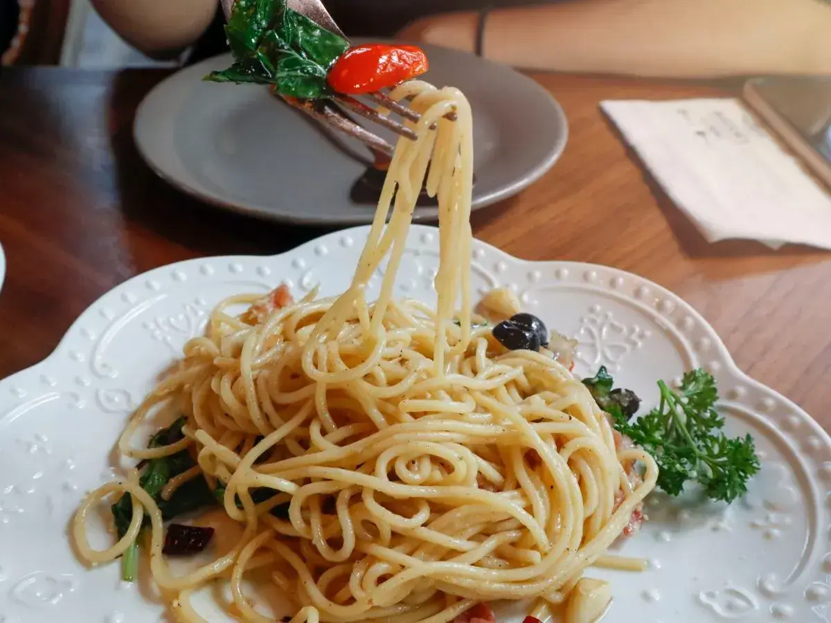 Widok z bliska na talerz pysznego spaghetti aglio olio, z widelcem unoszącym porcję makaronu, listkami bazylii i pomidorkiem.