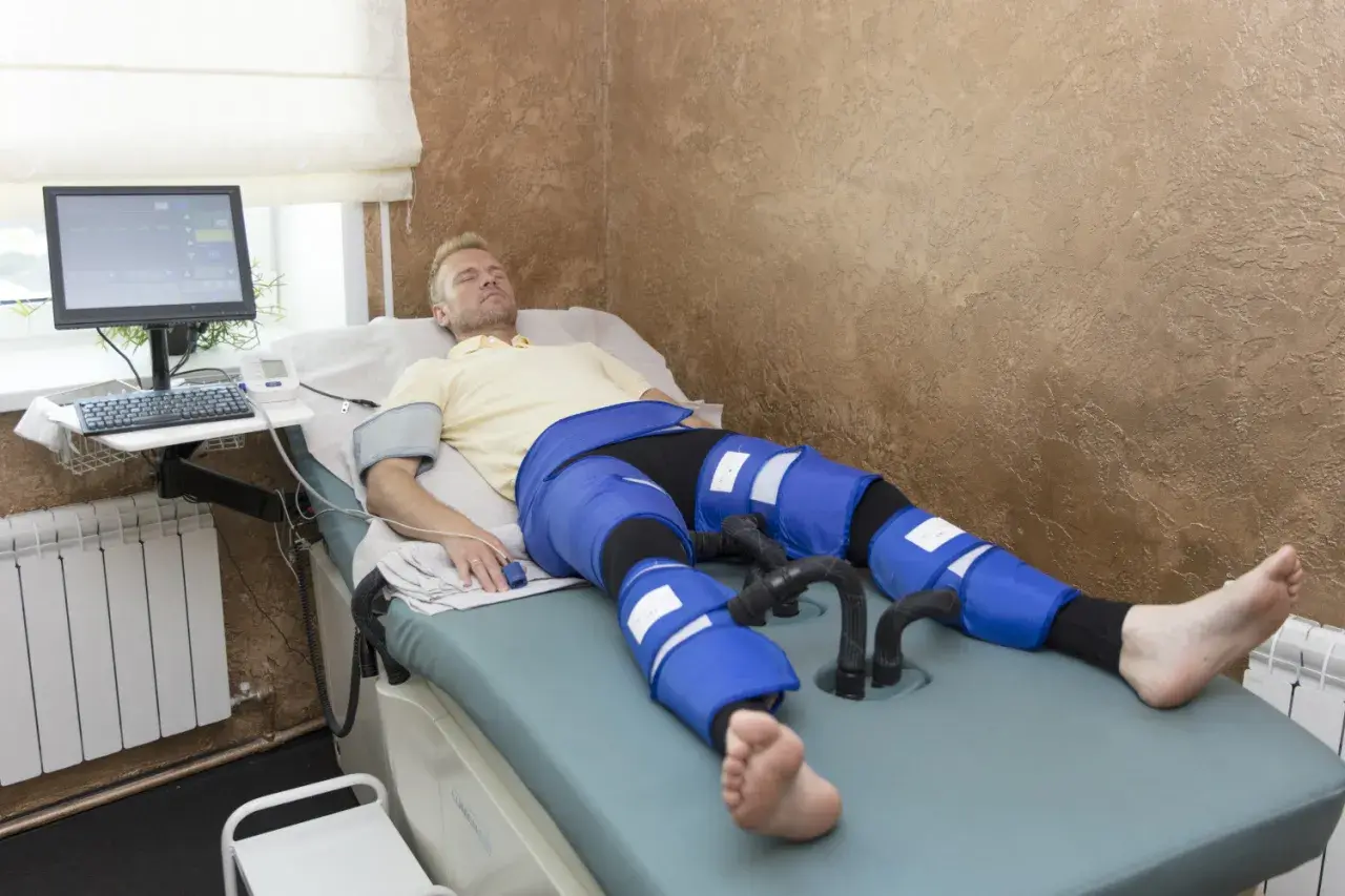 Mężczyzna leży na łóżku rehabilitacyjnym z założonymi rękawami do drenażu limfatycznego na nogach.