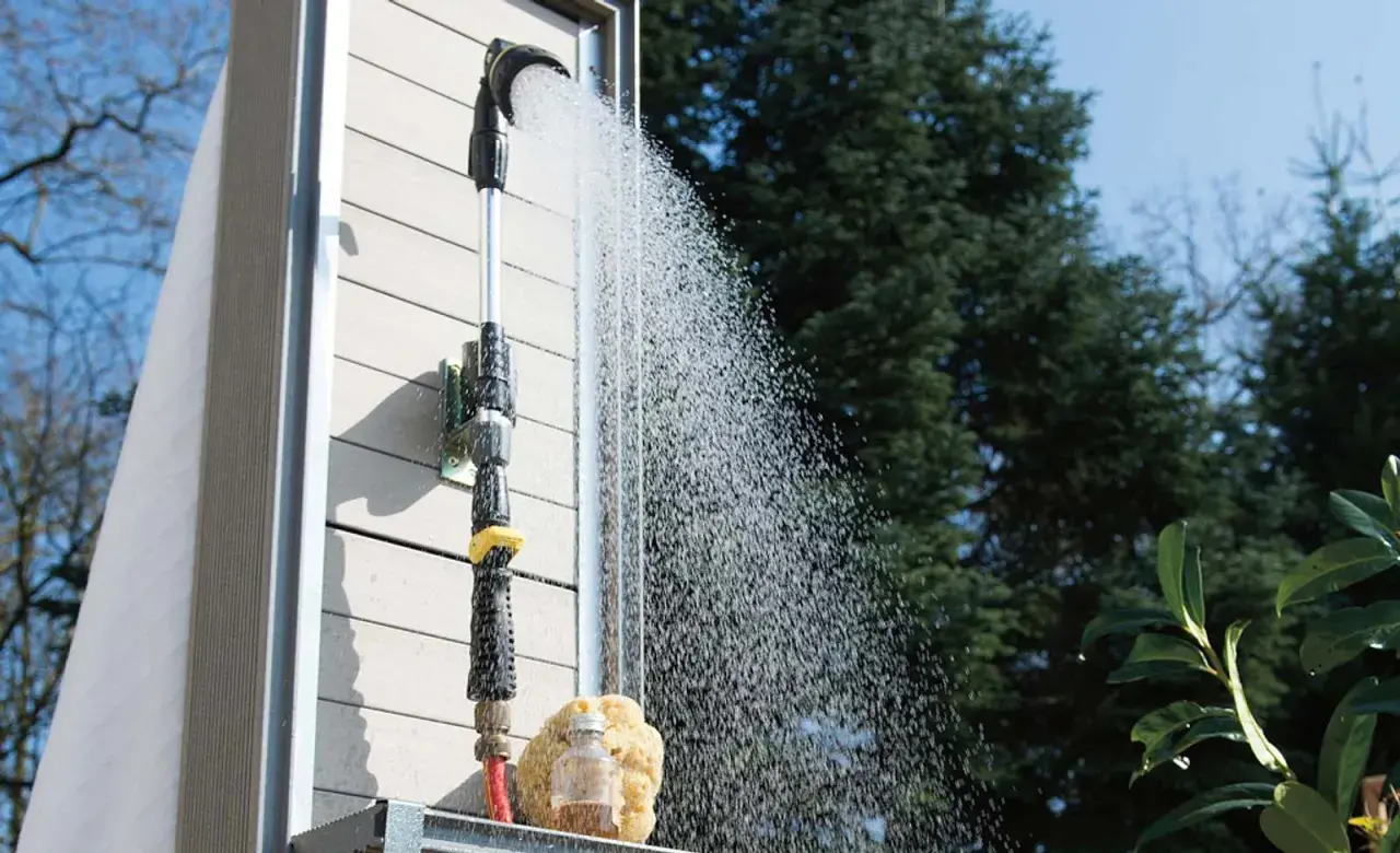 Eine Gartendusche, die man selber bauen kann, sprüht erfrischendes Wasser. Ein Schwamm und eine kleine Flasche stehen bereit.