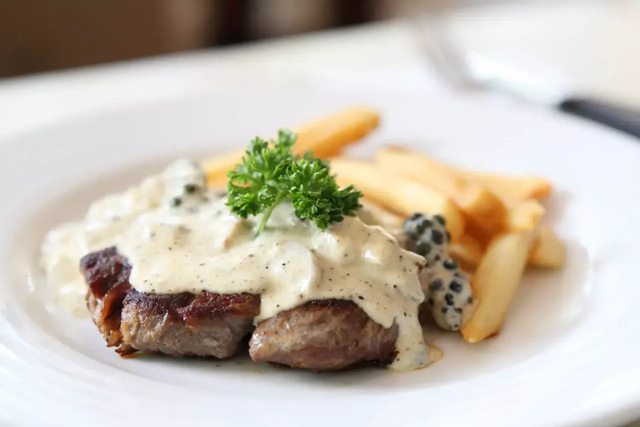 Filete de res bañado en cremosa salsa a la pimienta, acompañado de papas fritas y perejil fresco.