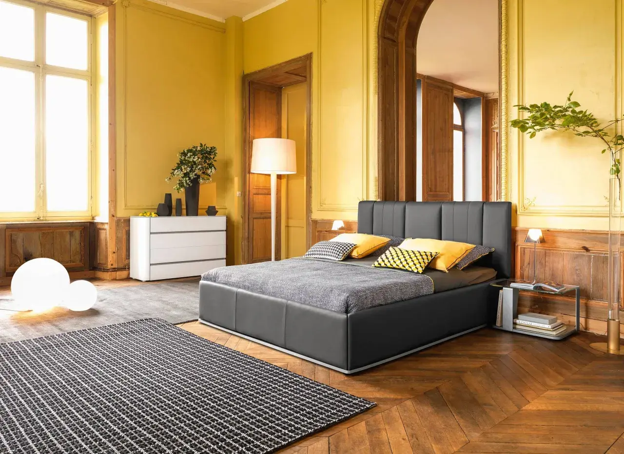 Camera da letto classica con pareti giallo ocra, letto grigio, tappeto a scacchi e arredi in legno.