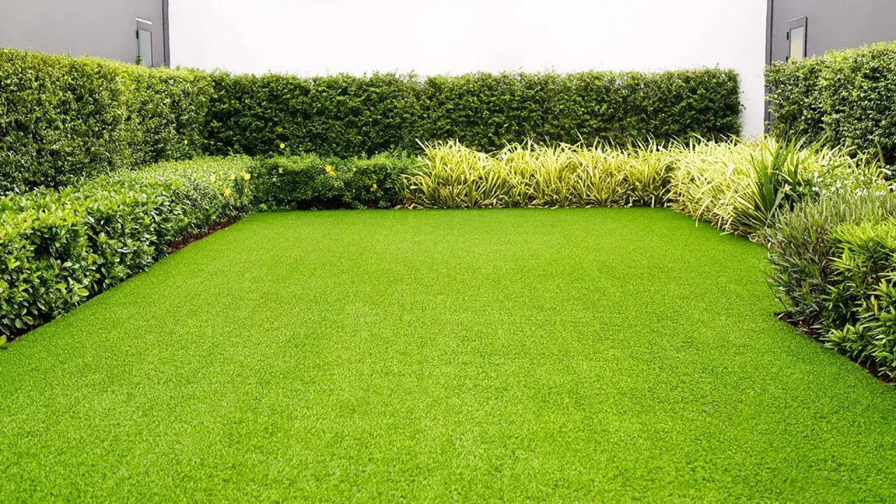 Un jardín impecable con césped artificial verde vibrante, rodeado de setos y plantas. Ideal para quienes buscan cual es el mejor césped artificial para jardín.