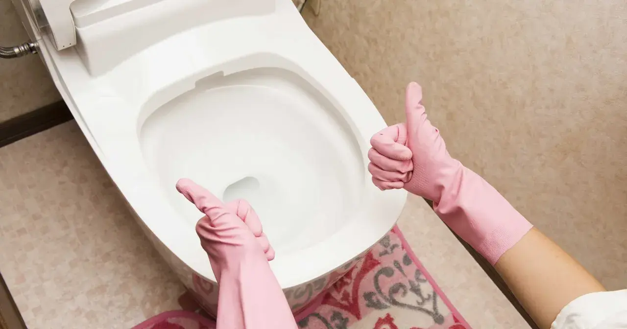 Ręce w różowych rękawiczkach pokazują kciuk w górę i wskazują na toaletę. Proste wskazówki, jak odetkać toaletę, gdy masz problem.