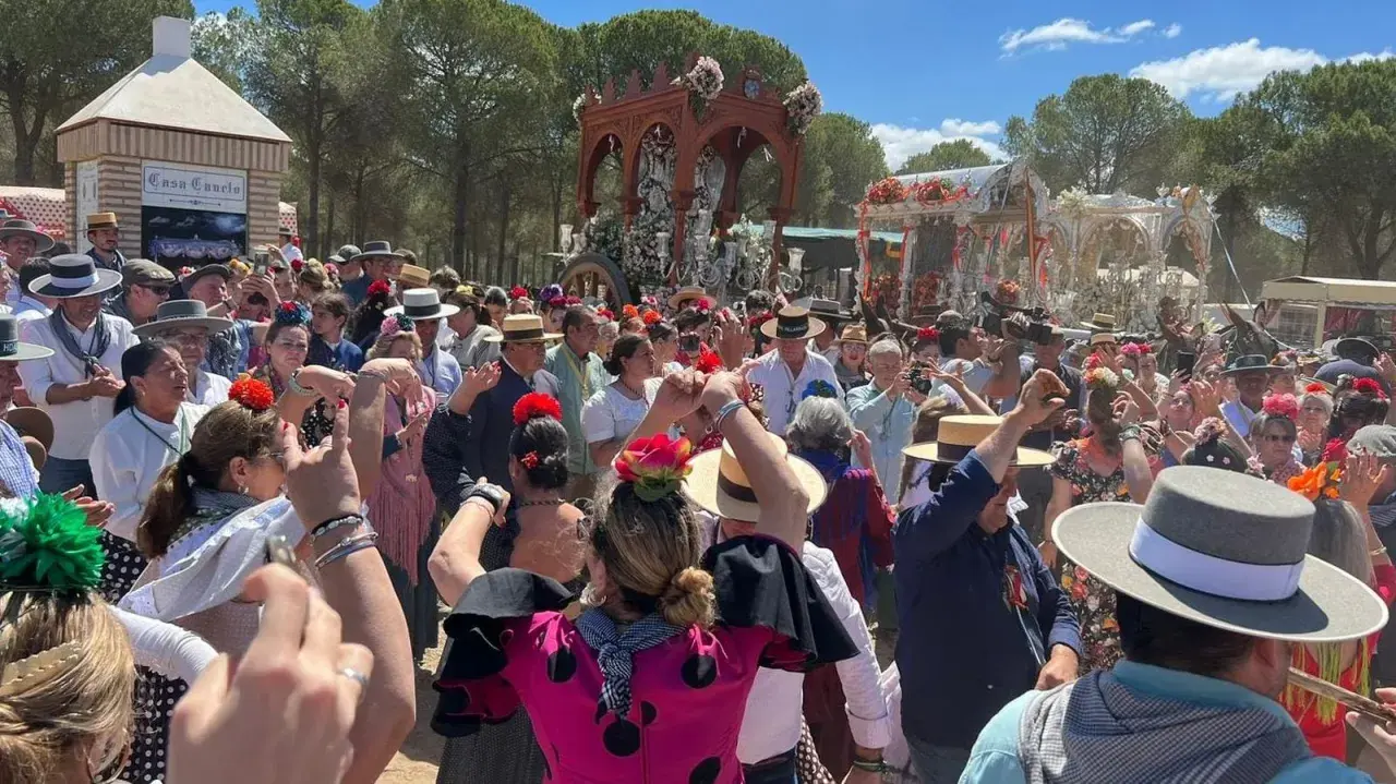 Multitud celebra con alegría, bailando y cantando al paso de una carreta adornada. Se percibe el espíritu de una sevillana rociera en pleno fervor.