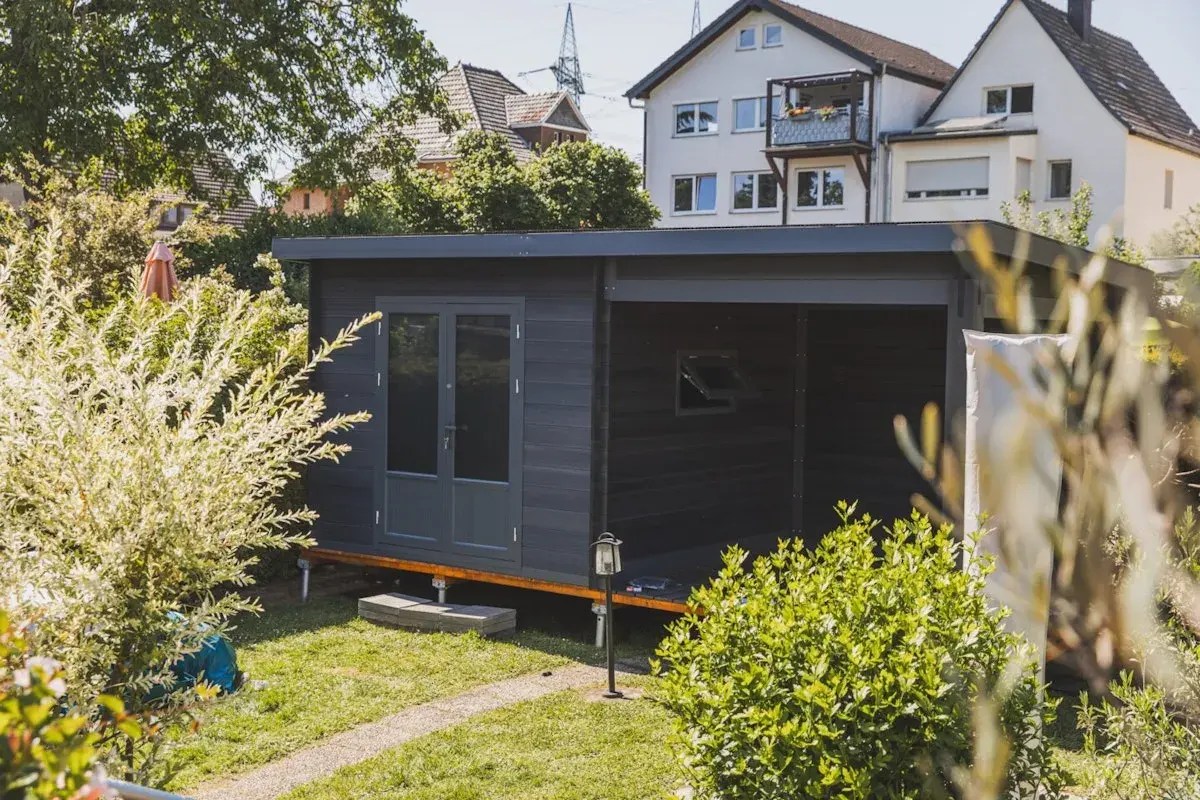 Modernes Gartenhaus mit Doppeltür und überdachter Veranda, ideal als Teil einer bauanleitung gartenhaus. Umgeben von üppigem Grün.