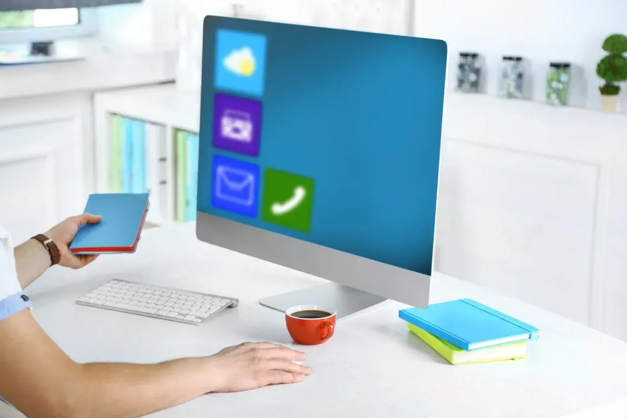 Pracownik biurowy z notatnikiem w dłoni, przed monitorem z ikonami aplikacji, jak w WPS Office.