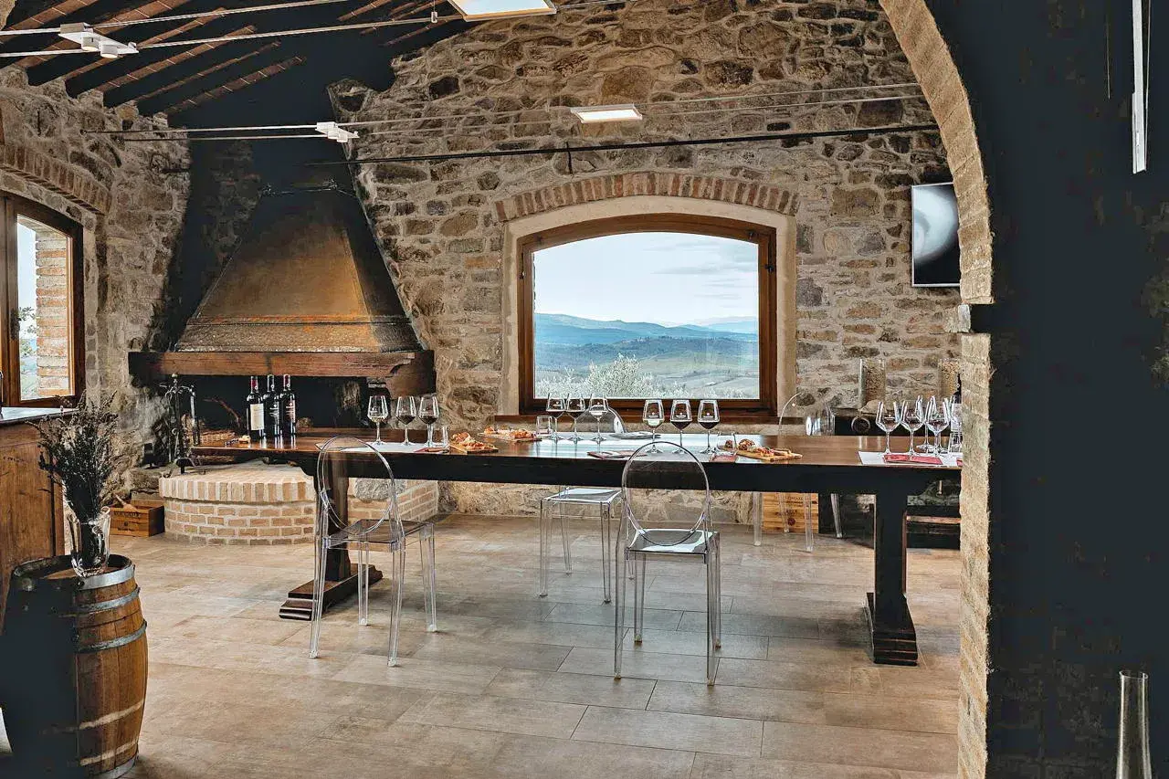 Sala degustazione in pietra con camino, tavola apparecchiata per assaggio vini, vista panoramica sulle colline del Chianti.