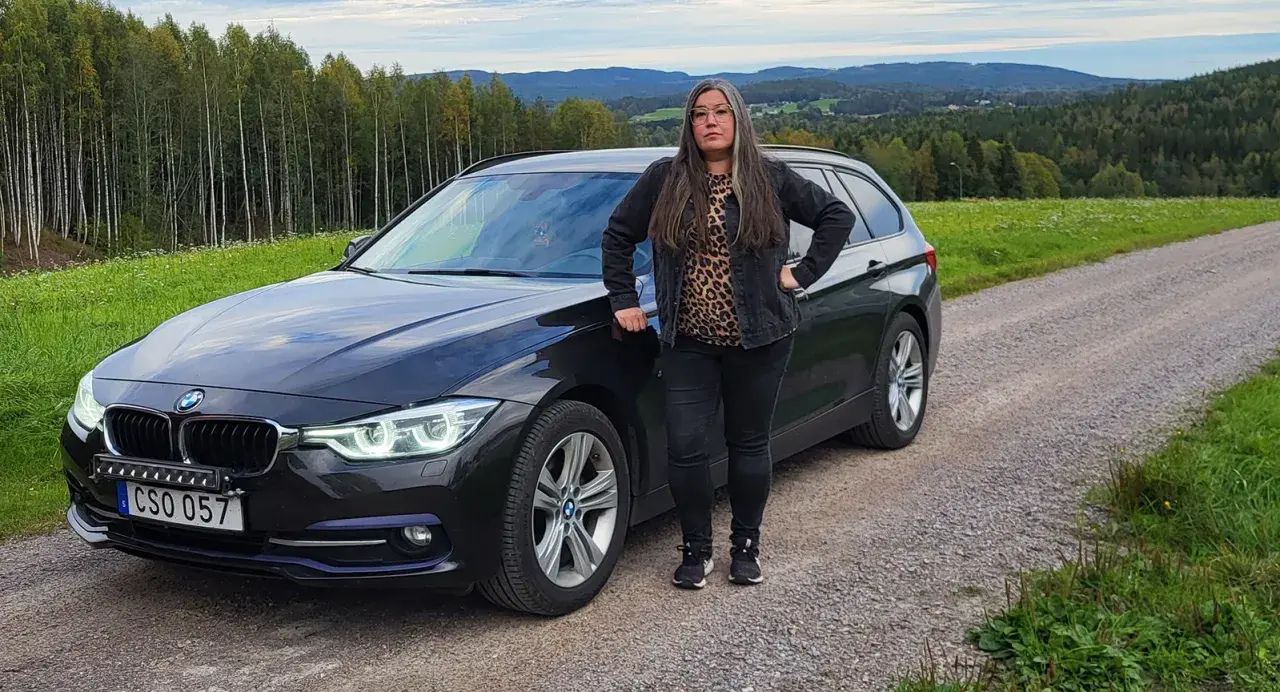 Kvinna vid en svart BMW kombi i svensk landsbygd. Kanske ett bmw b47 problem som gör att hon stannat här.