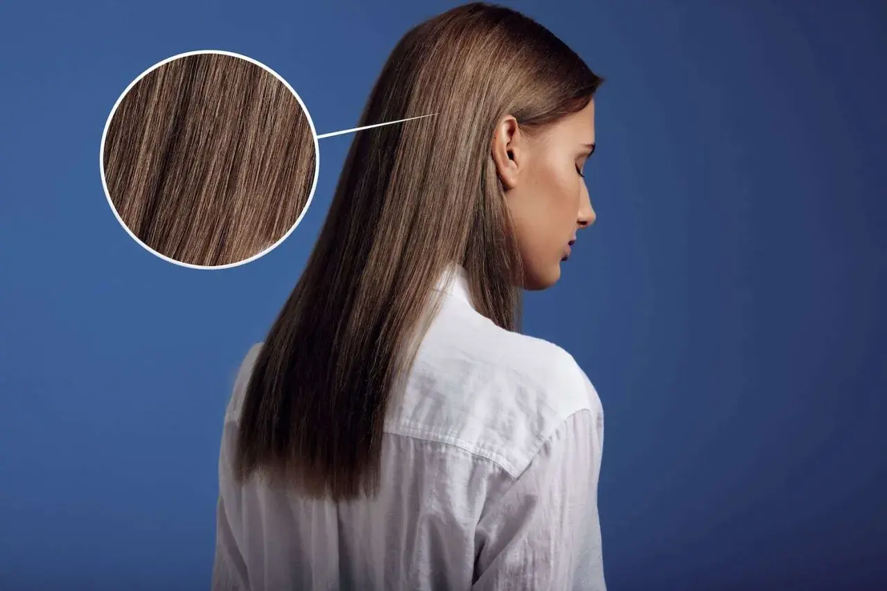 Primer plano de un cabello castaño sedoso, con un círculo que amplía los detalles. Parece que el pelo está en pausa, esperando un nuevo estilo.