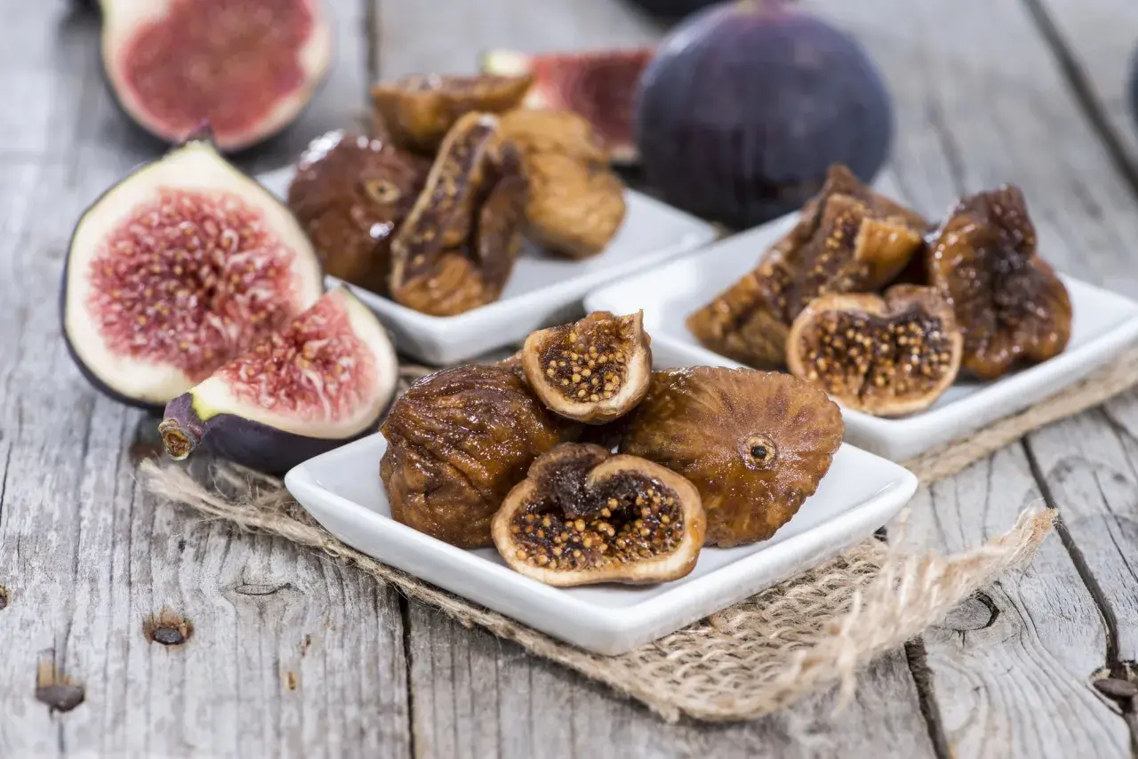 Des figues fraîches et des figues séchées au four sur des assiettes blanches, posées sur du bois rustique.