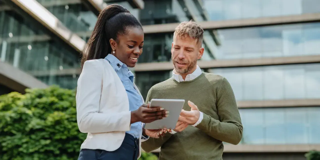 Two professionals discuss their MPA online program on a tablet outside a modern building.