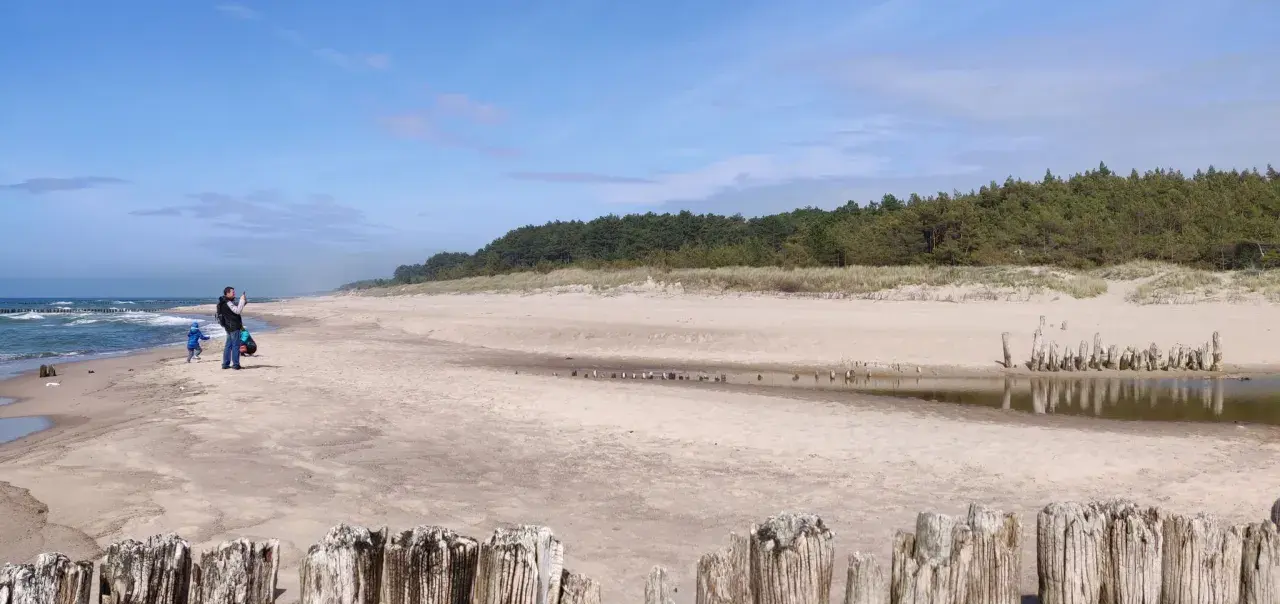Piękna plaża w Dąbkach, idealne miejsce na rodzinne atrakcje. Ojciec z dzieckiem spacerują brzegiem morza.