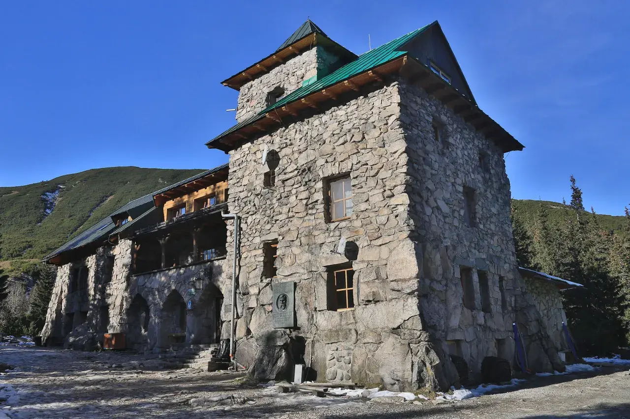 Kamienny budynek schroniska w Tatrach Polskich, z zielonym dachem i widokiem na górzyste tereny.