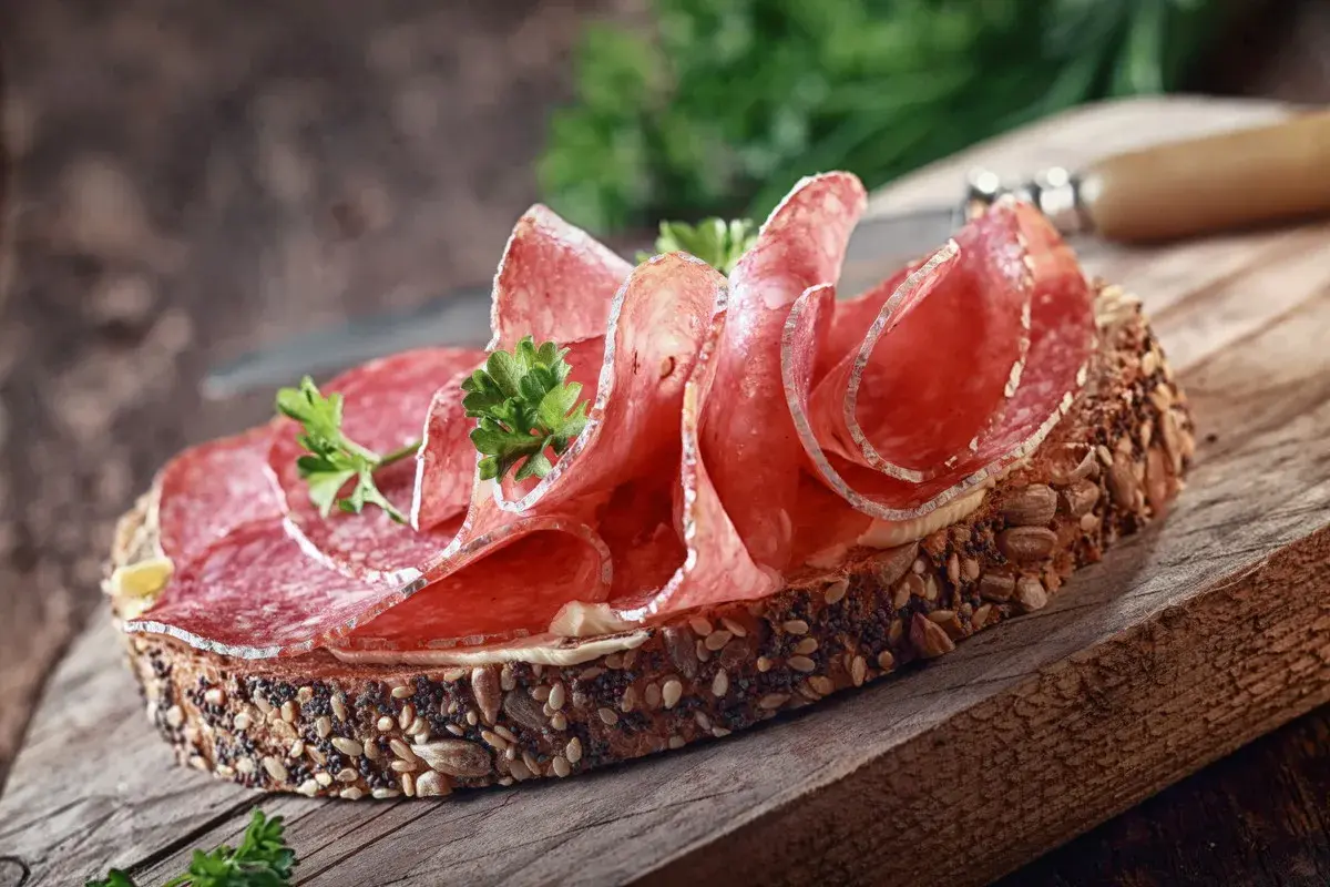 Kanapka z ciemnego pieczywa obficie posypanego ziarnami, z plasterkami aromatycznego salami i natką pietruszki.