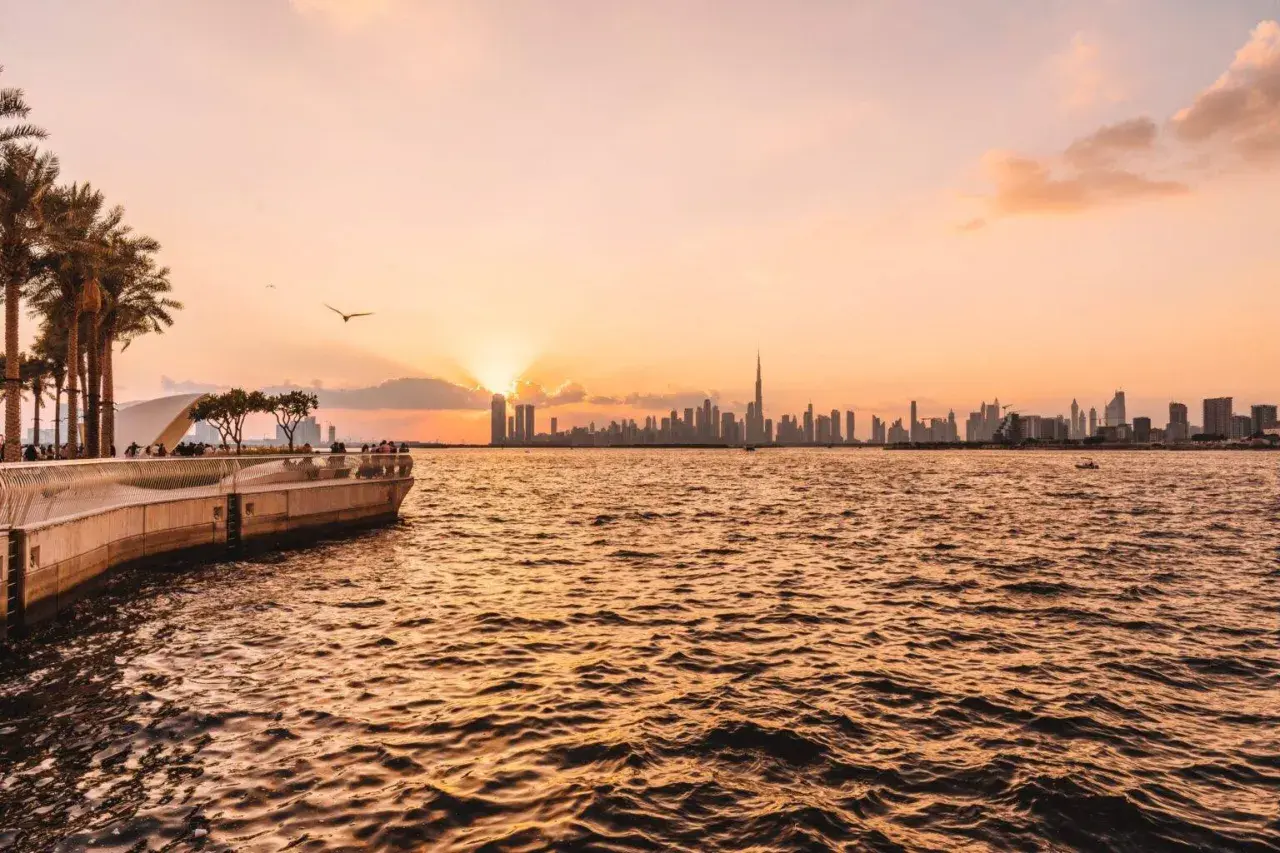 Sonnenuntergang über Dubai. Die Skyline mit dem Burj Khalifa und Palmen am Ufer sind einige der Dubai Highlights.