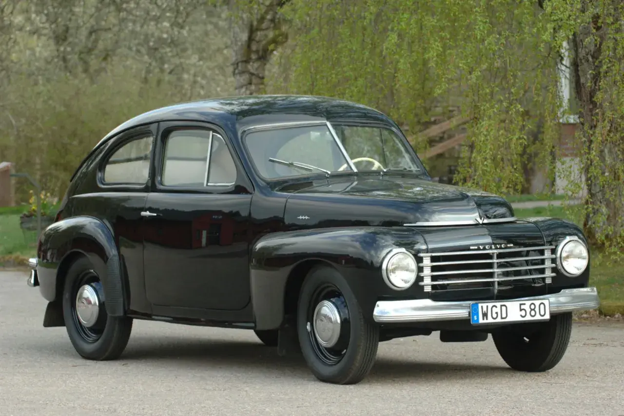 Svart Volvo PV 1954, en klassisk svensk bil, parkerad utomhus med grönska i bakgrunden.