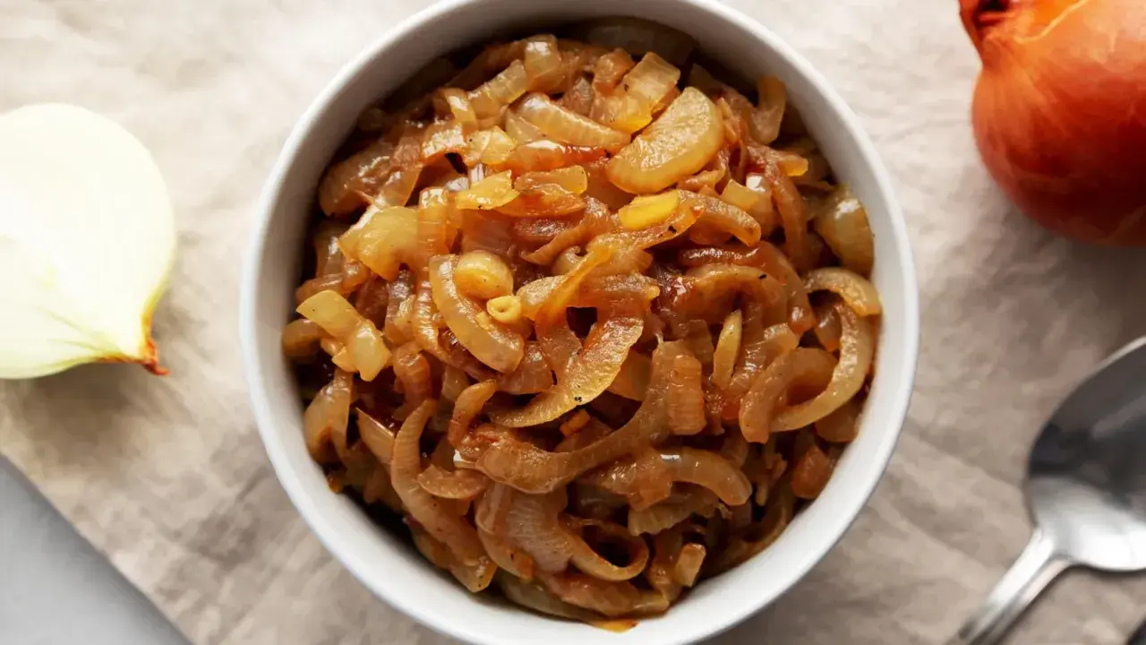 Un bol rempli d'oignons caramélisés dorés, parfaits pour une recette savoureuse. Un oignon cru à côté.