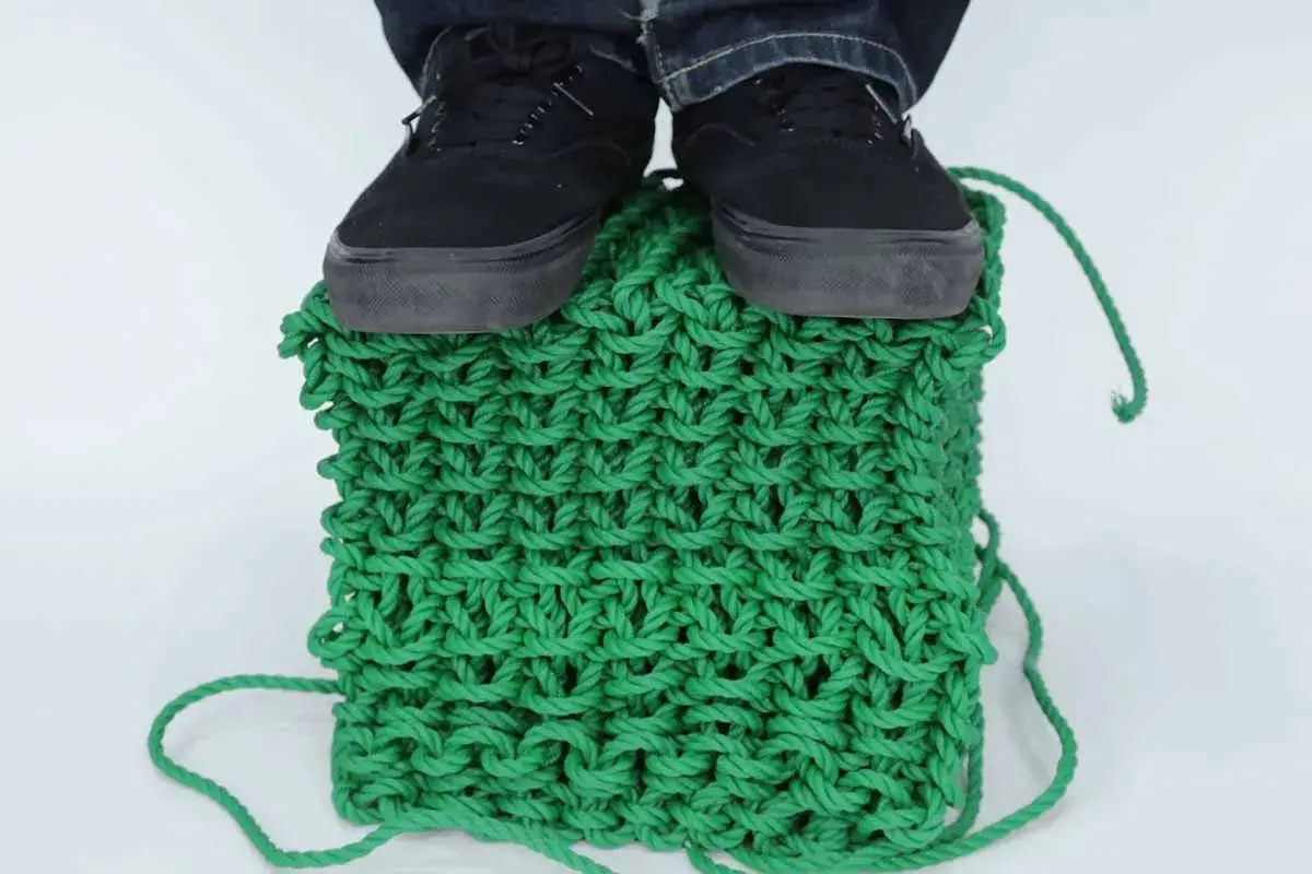 Pieds chaussés sur un cube de tricotage 3D vert vif, démontrant la solidité de la maille.