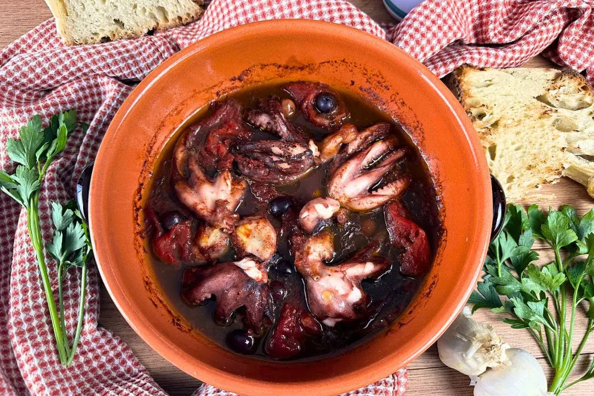 Polipetti alla luciana in terracotta, con pomodoro, olive e pane tostato.