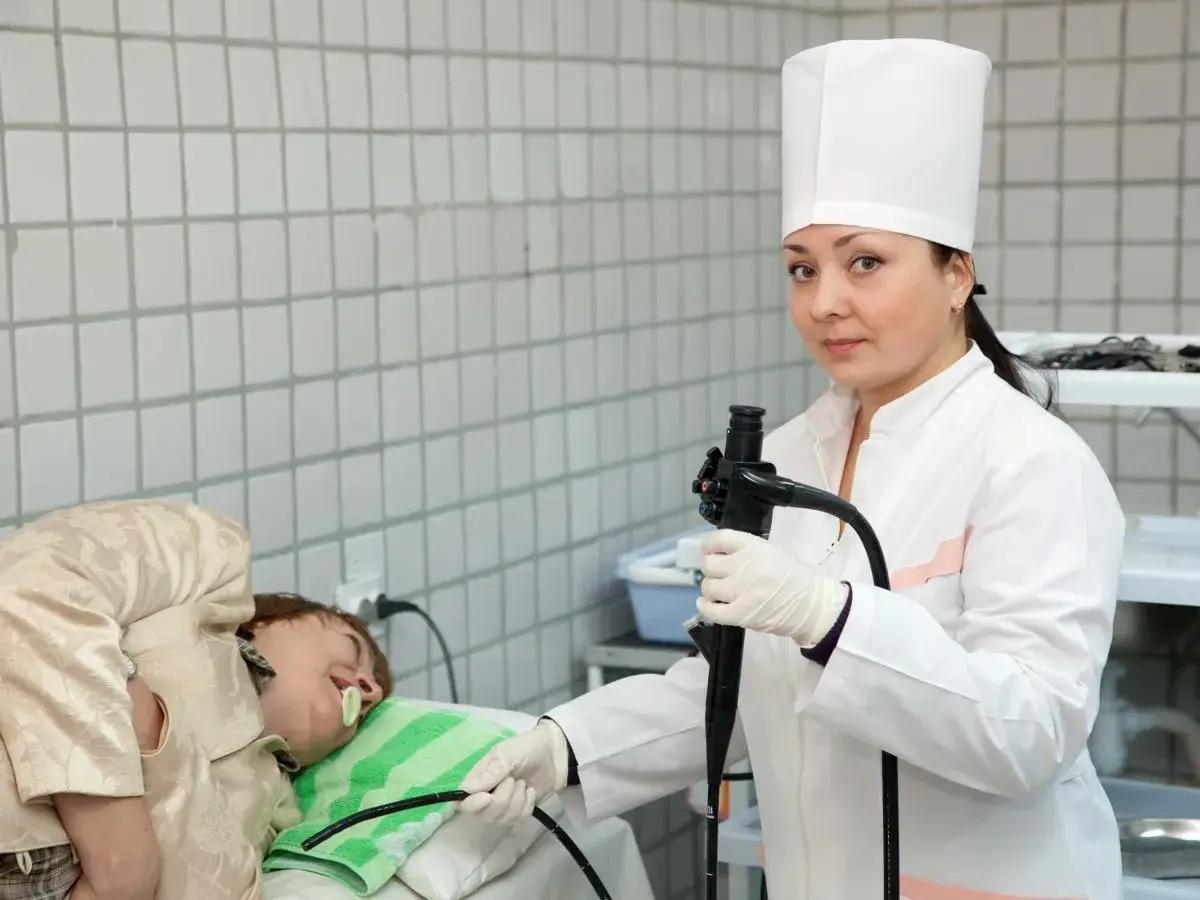 Lekarka w białym kitlu przygotowuje pacjenta do gastroskopii, trzymając endoskop.