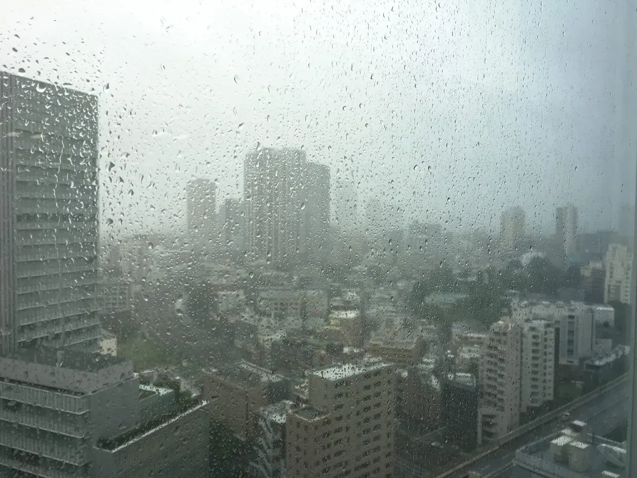Regen prasselt auf ein Fenster mit Blick auf eine Stadt in Japan. Die Sicht ist durch die Tropfen und den grauen Himmel getrübt, typisch für die japan taifun saison.