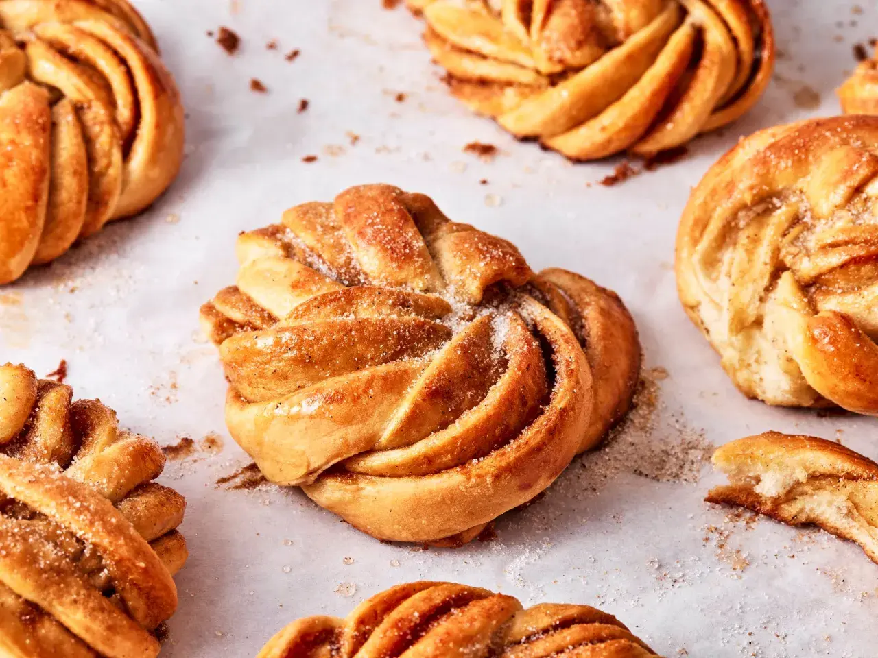 Goldbraune Kardamomschnecken, bestreut mit Zucker und Zimt, liegen auf Backpapier.