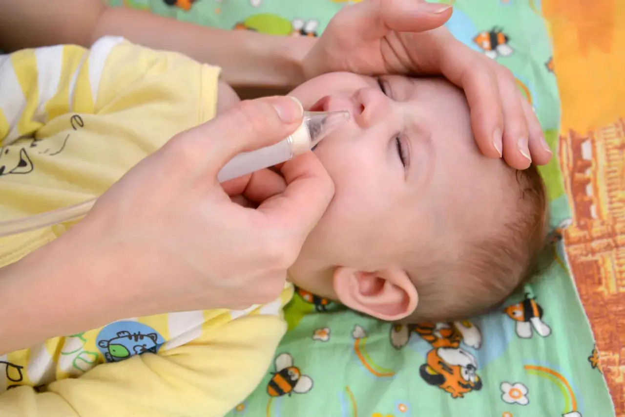 Mani delicate aiutano un neonato di 1 mese con il raffreddore, usando un aspiratore nasale per liberare il piccolo nasino.