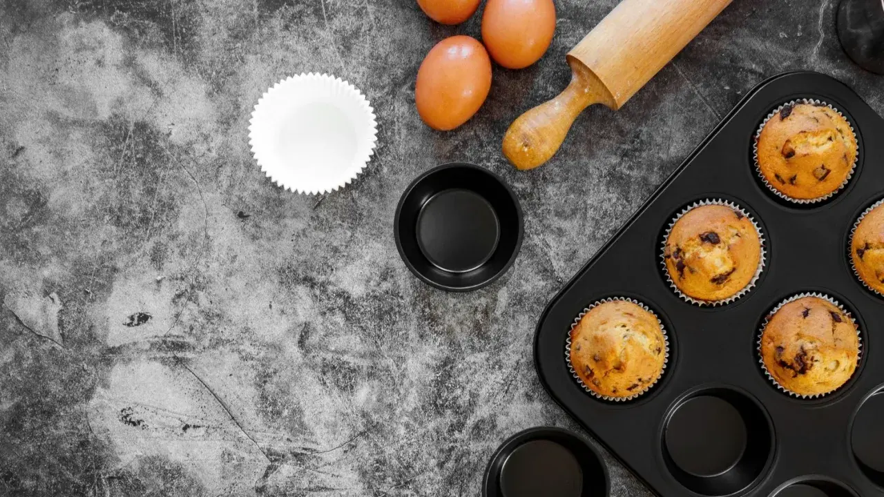 Gotowe muffinki w foremkach do ciast, jajka i wałek do ciasta na kamiennym blacie.