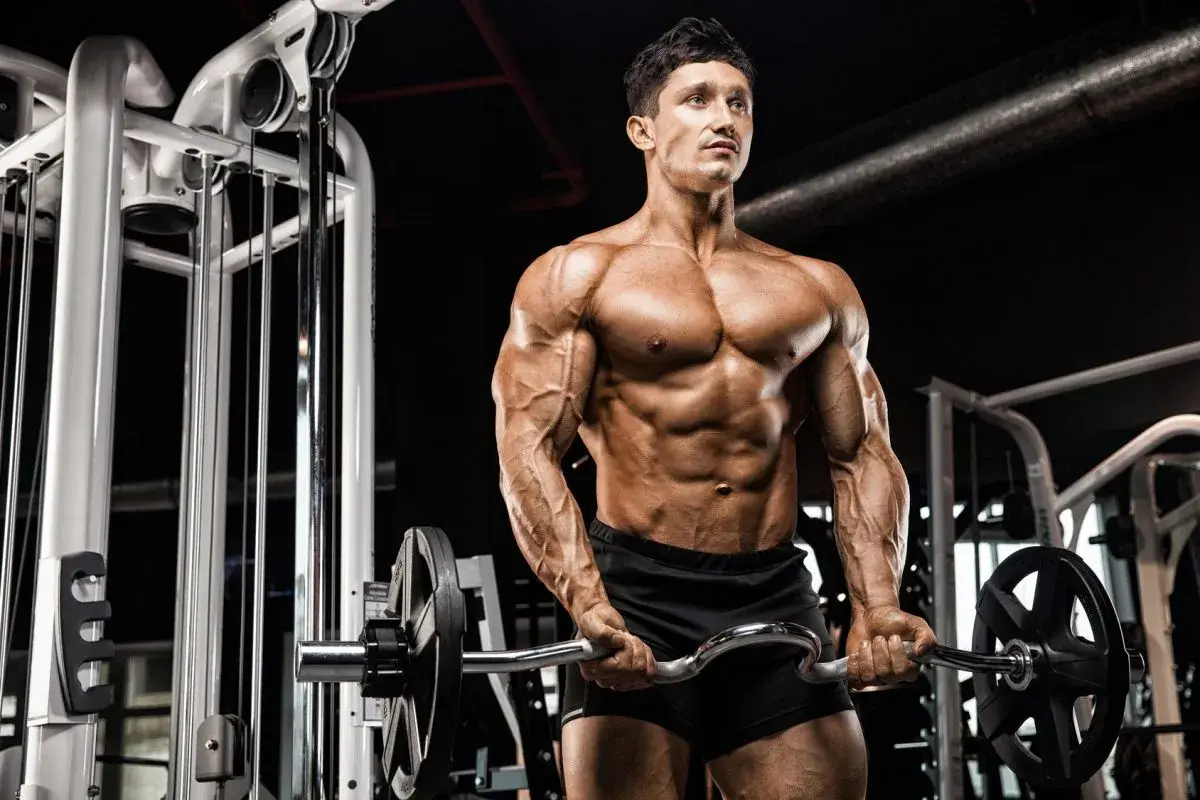 Mężczyzna z wyrzeźbionym ciałem wykonuje ćwiczenia na biceps z łamaną sztangą w siłowni.