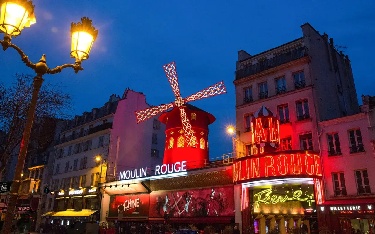 Le Moulin Rouge illuminé la nuit. La durée du spectacle est une question que beaucoup se posent avant de venir admirer ce lieu emblématique.