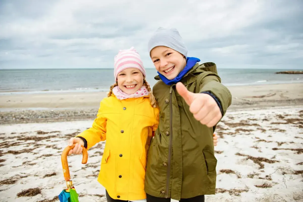 Zwei Kinder am Strand, bereit für Abenteuer, egal was kann man bei schlechtem Wetter machen.