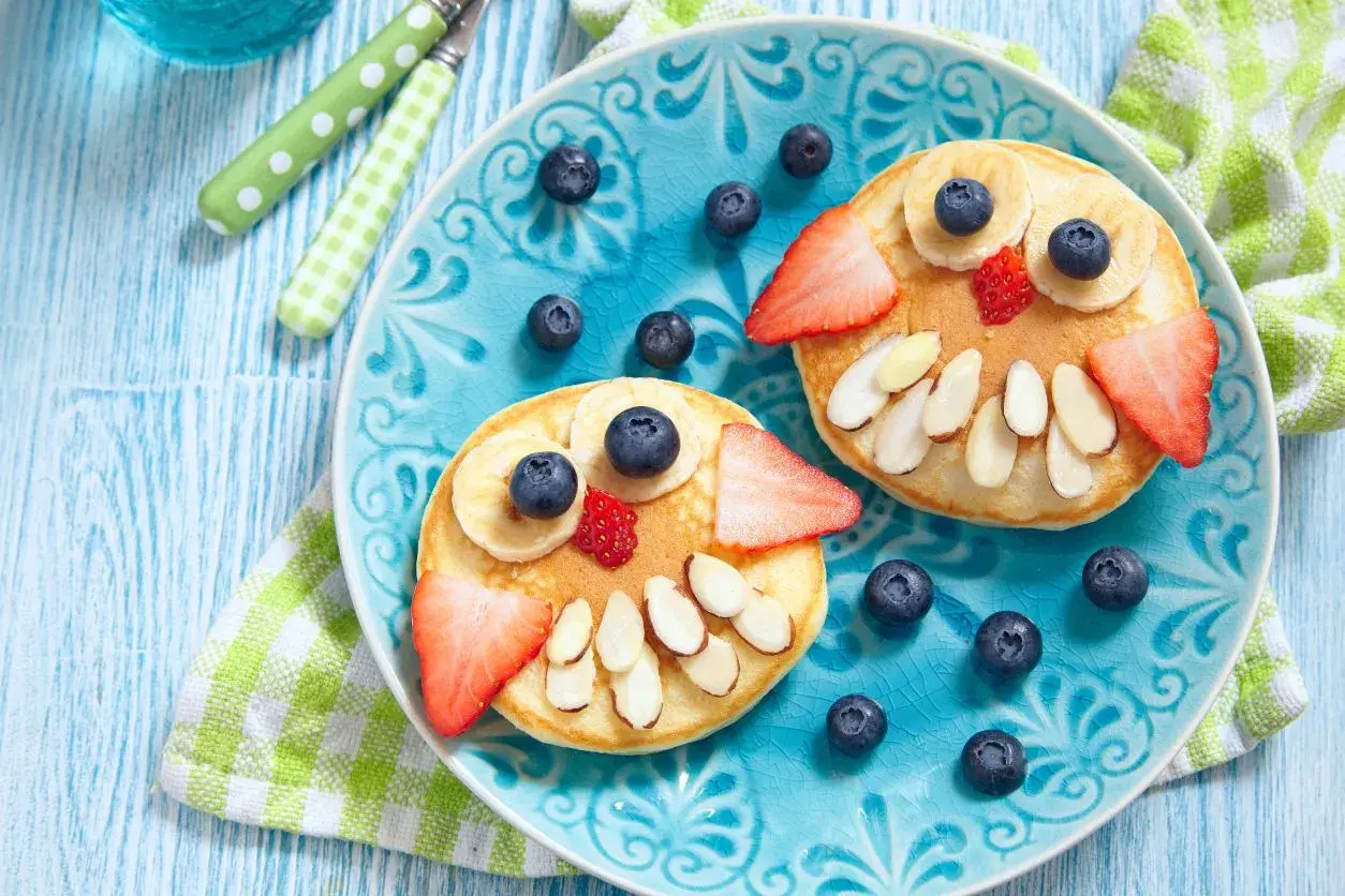 Due pancake a forma di gufo, decorati con frutta e mandorle, per una colazione sana bambini.