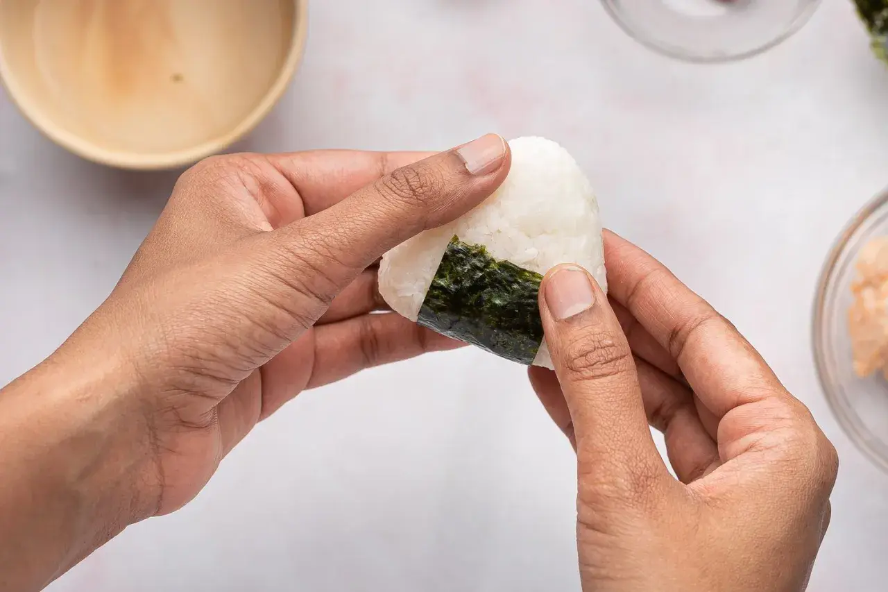 Hands shaping a perfectly sized onigiri, a delicious rice ball wrapped in nori seaweed.