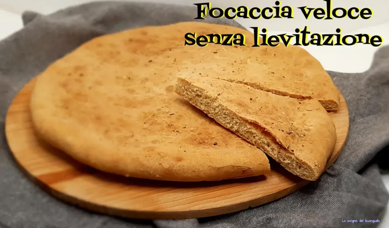 Focaccia veloce senza lievitazione su tagliere di legno. Una fetta è stata tagliata per mostrare la morbidezza.