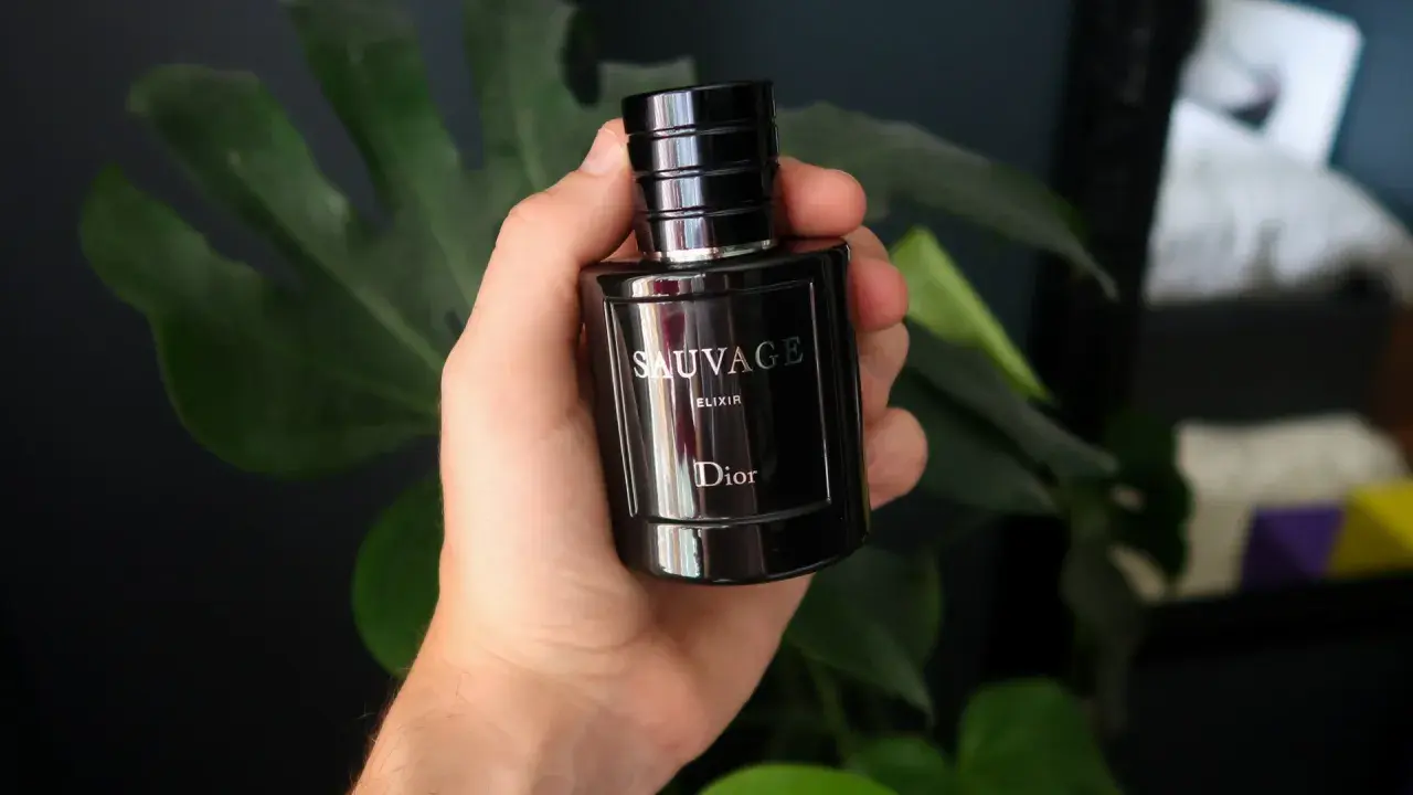 Dłoń trzyma flakon Dior Sauvage Elixir 60ml, otoczony zielonymi liśćmi.