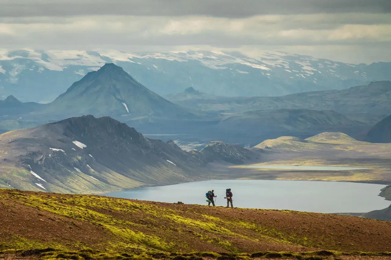 Two hikers on a self-guided Laugavegur trail adventure, with a serene lake and dramatic mountains in the background.