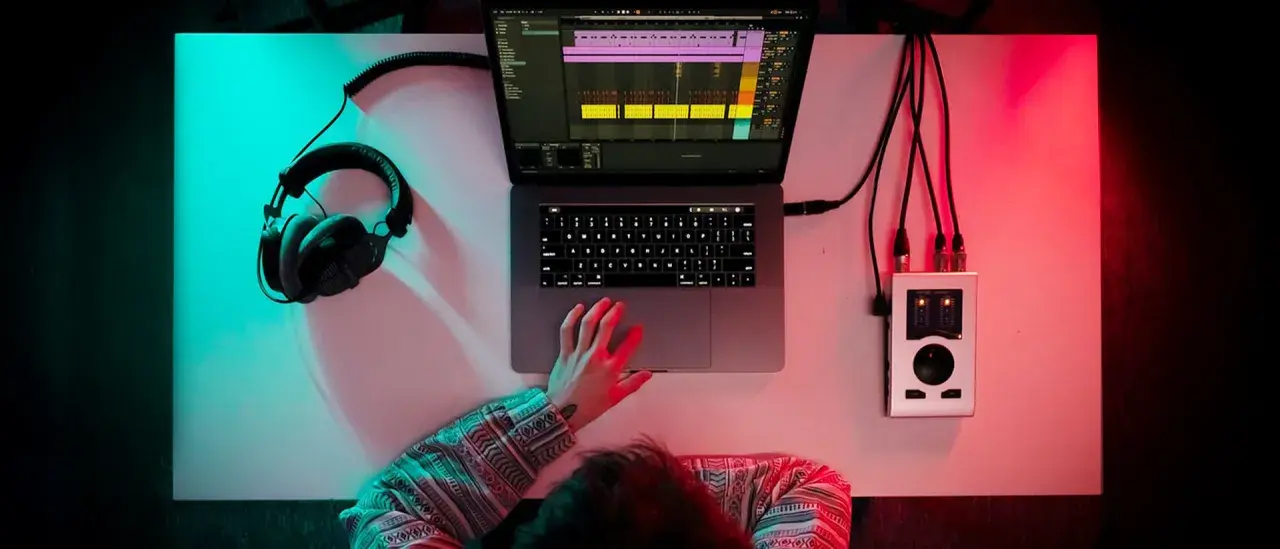 Person am Schreibtisch, um einen Beat zu machen, mit Kopfhörern, Laptop und Audio-Interface.