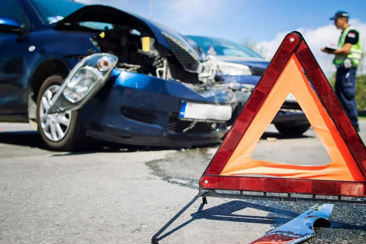 Triangolo di emergenza davanti a due auto danneggiate dopo un incidente. Un poliziotto documenta i danni, forse un incidente senza assicurazione.