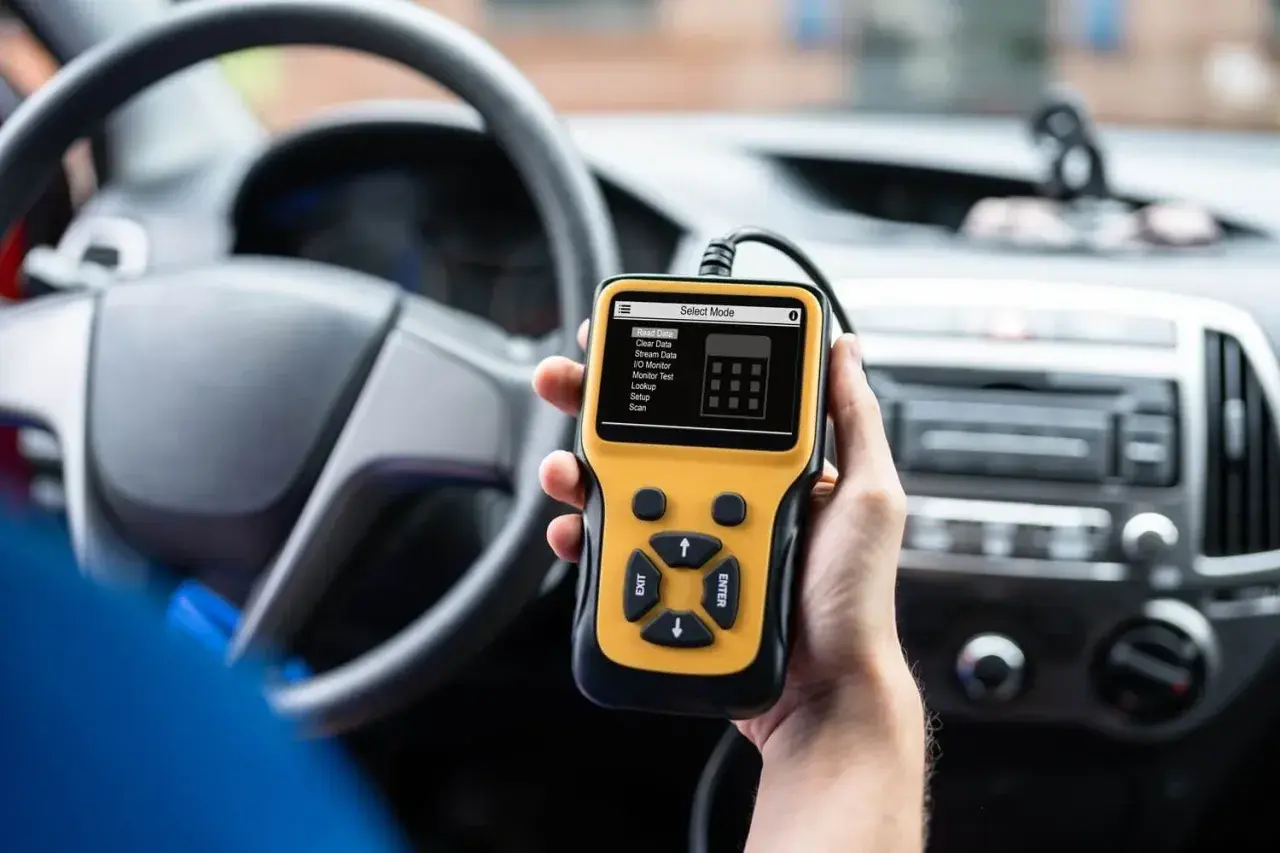 Ręka trzyma żółty skaner diagnostyczny OBD2 w samochodzie, gotowy do porównania z OBD1.