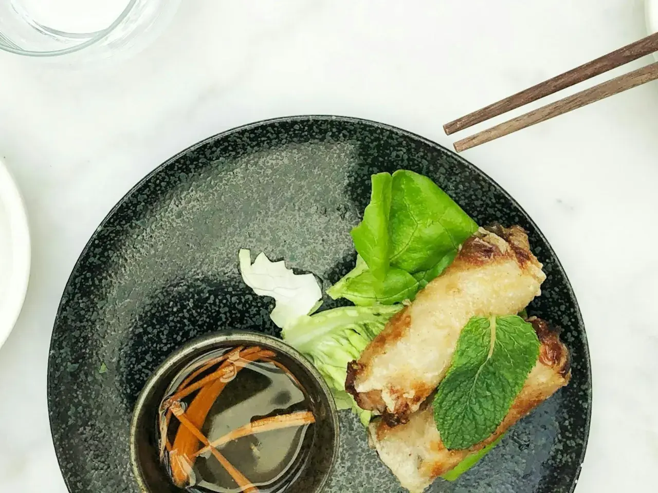 Deux nems dorés sur un lit de salade, accompagnés d'une coupelle de sauce nem maison et de baguettes.