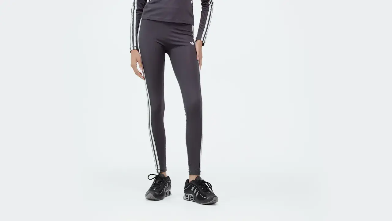Leggings Adidas 3 stripes grigi, con logo e strisce bianche, abbinati a sneakers nere.