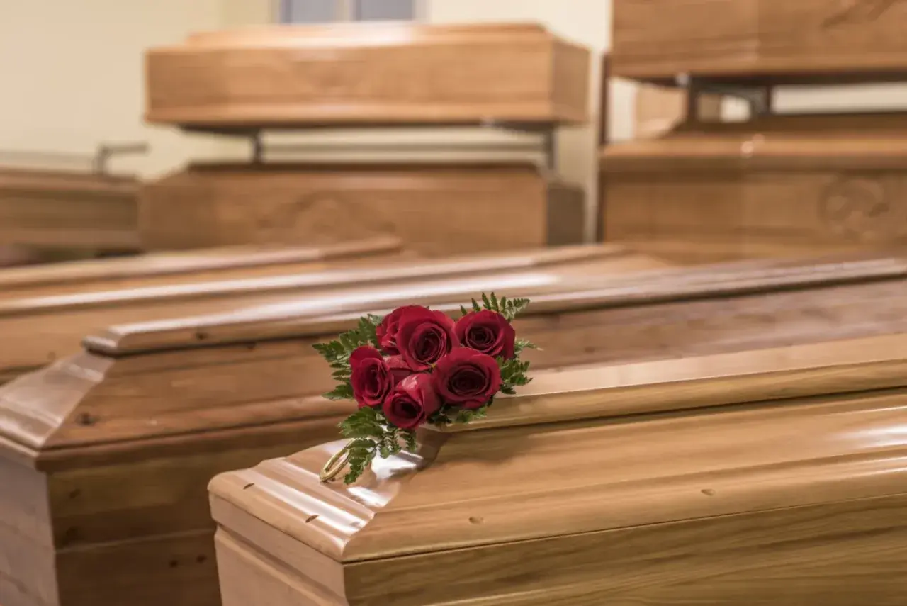 Wiele rodzajów trumien, niektóre ułożone piętrowo. Na jednej z nich bukiet czerwonych róż i złota obręcz.