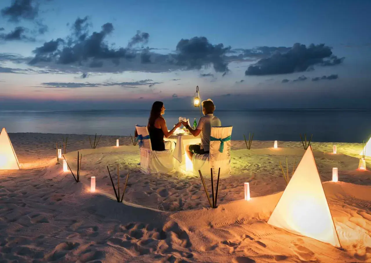 Romantyczna kolacja na plaży. Para świętuje 4 rocznicę ślubu przy blasku lampionów i zachodzącego słońca.