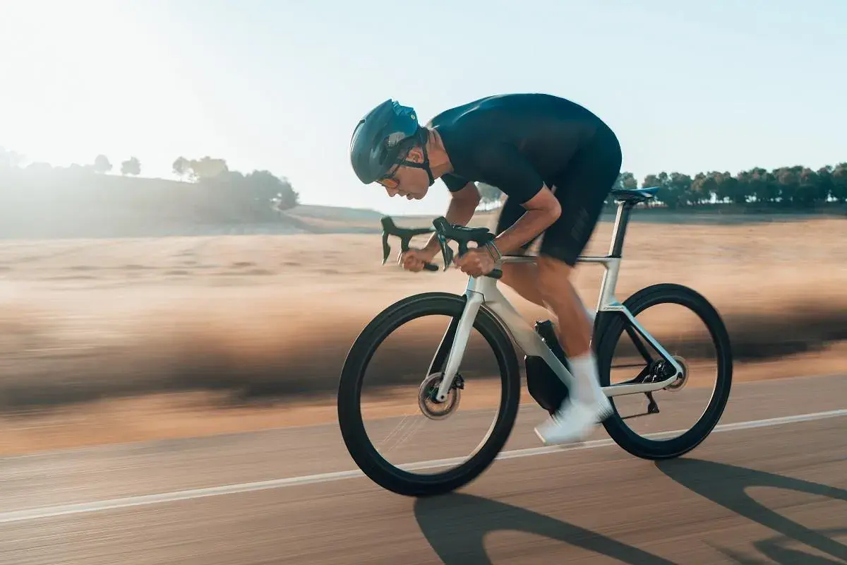 Kolarz w aerodynamicznej pozycji minimalizuje opory toczenia opon rowerowych, pędząc przez krajobraz.